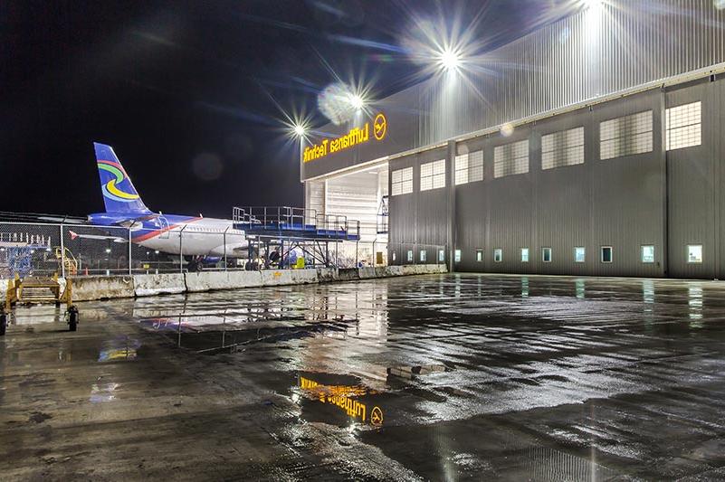 Exterior of Lufthansa Technik Heavy Maintenance Facility at night. Airplane entering hangar in the back.